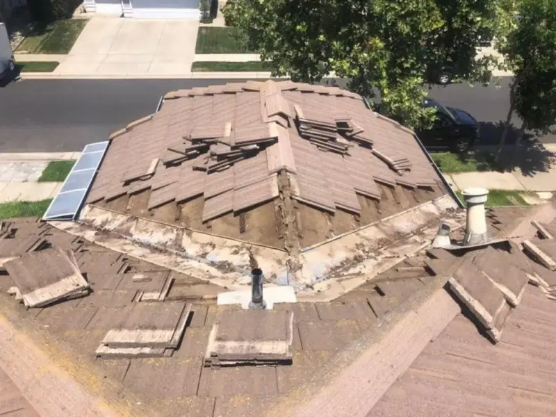 Concrete tile roof with lifted tiles exposing worn valley and hip flashing