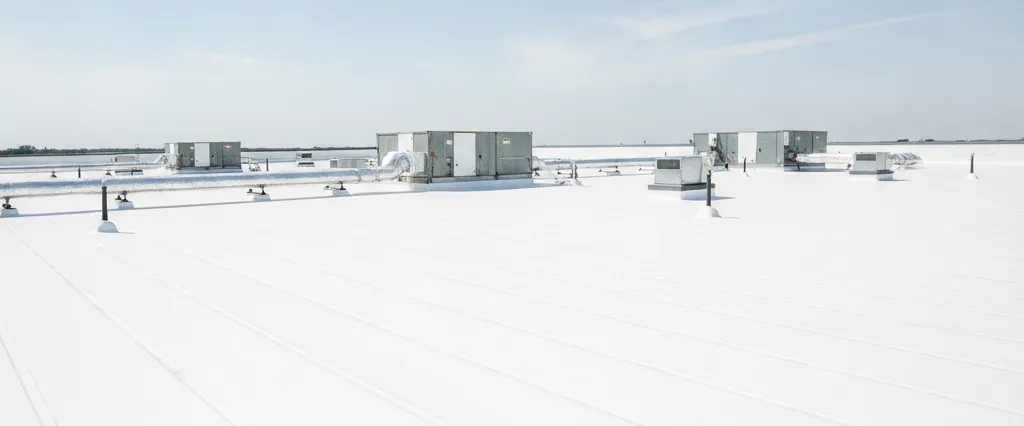Wide view across a low-slope commercial building rooftop with a white membrane and rooftop units under a clear sky