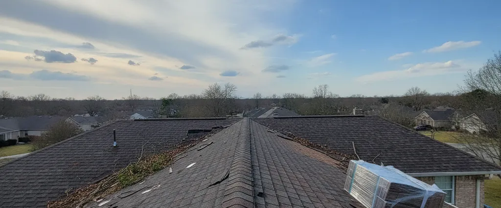 Residential rooftop after a storm with wind and hail damage being repaired, new shingles staged, clear post-storm sky
