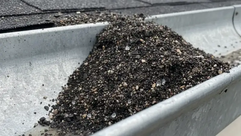 Asphalt granules washed into a gutter after a hailstorm indicating shingle impact