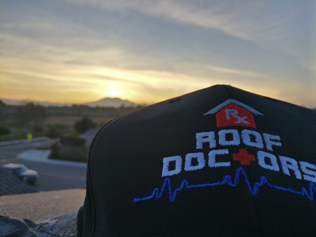 close-up of a hat with the roof doctors logo on it overlooking a beautiful sunset
