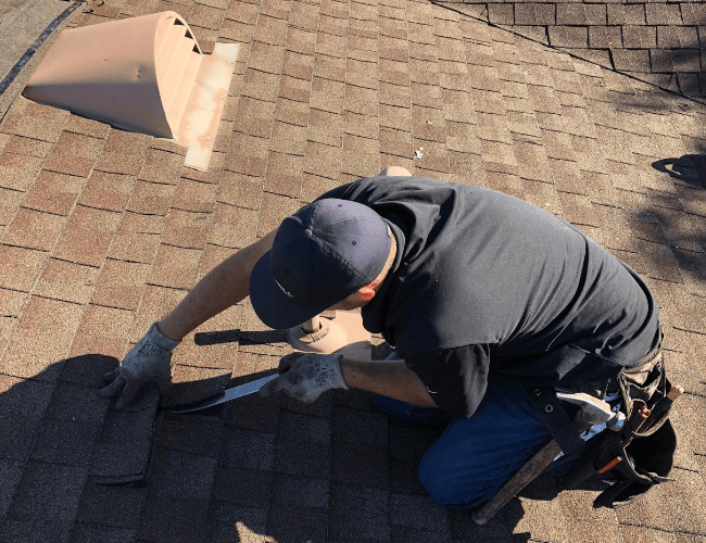 a man kneeling down on a shingle roof during a roof repair