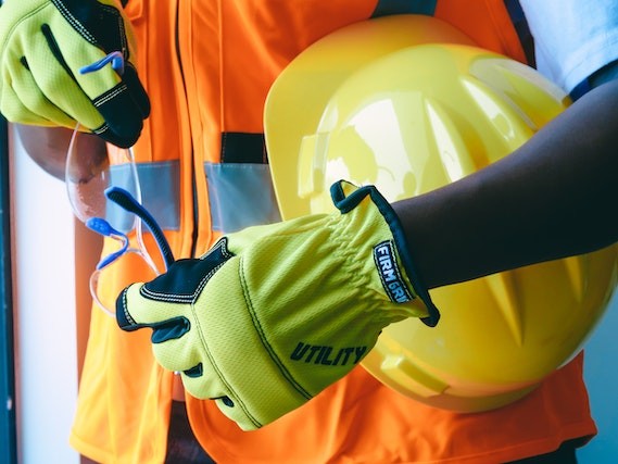 close-up of a contractor holding a yellow helmet holding safety glasses and in orange reflective vest